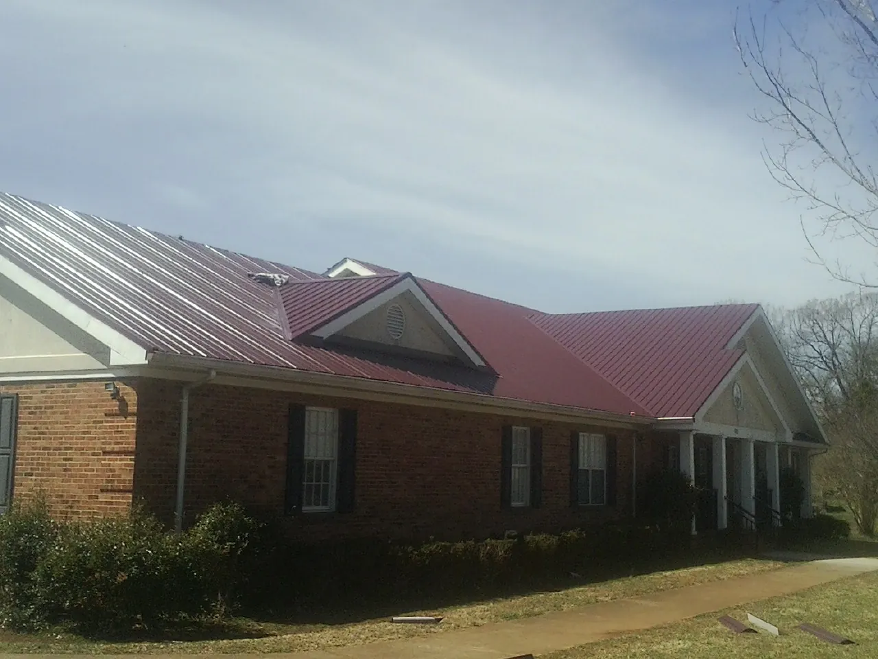 Red metal roof with gabled entries on a long brick building, from a Hail Damage Roof Repair job in Otley