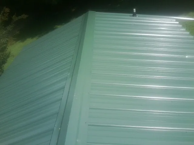 New green metal panels meeting at the ridge of a roof — Flat Roof Repair work by our crew in Otley