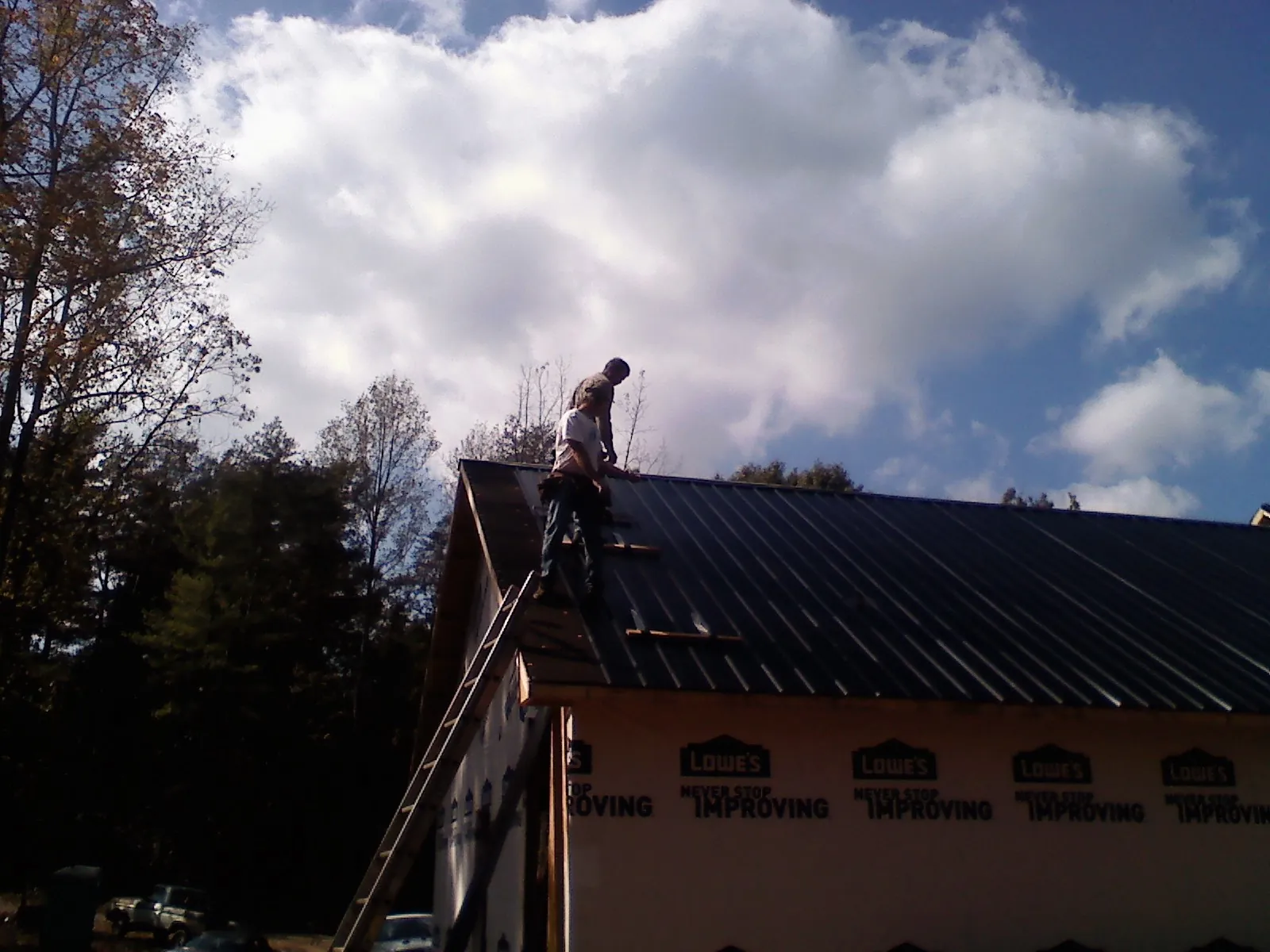 Roofer fastening dark metal panels high against a cloudy sky, from a Roof Inspection job in Otley