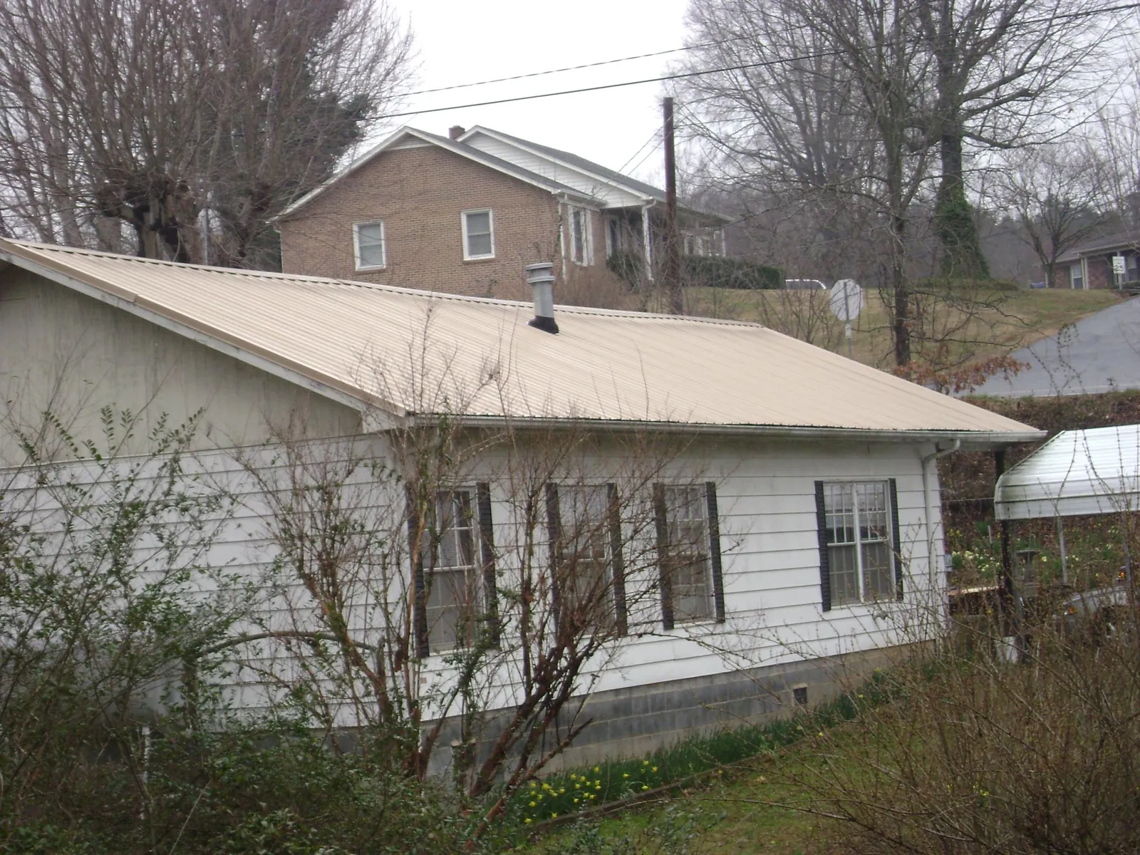 Tan metal roof on a white sided house set into a hillside — Commercial Roofing by Roofing Brothers in Otley