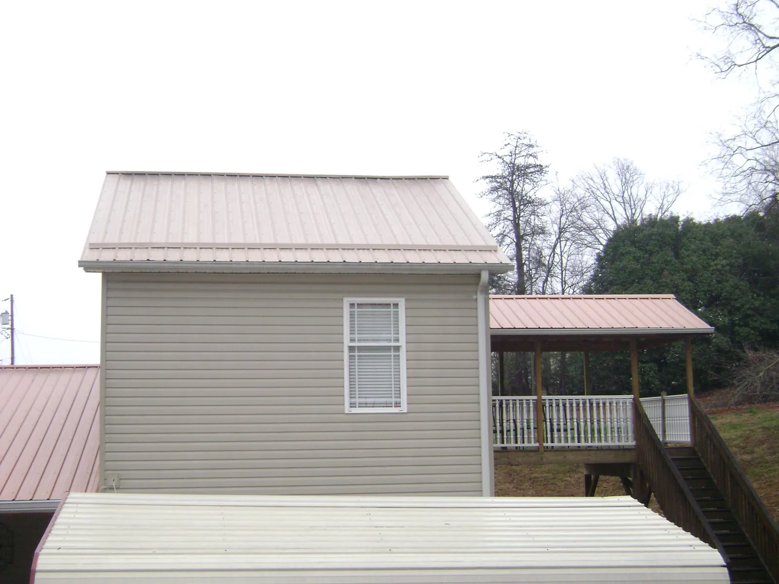 Tan metal roofs on a two story addition and attached porch, from a Roof Replacement job in Otley